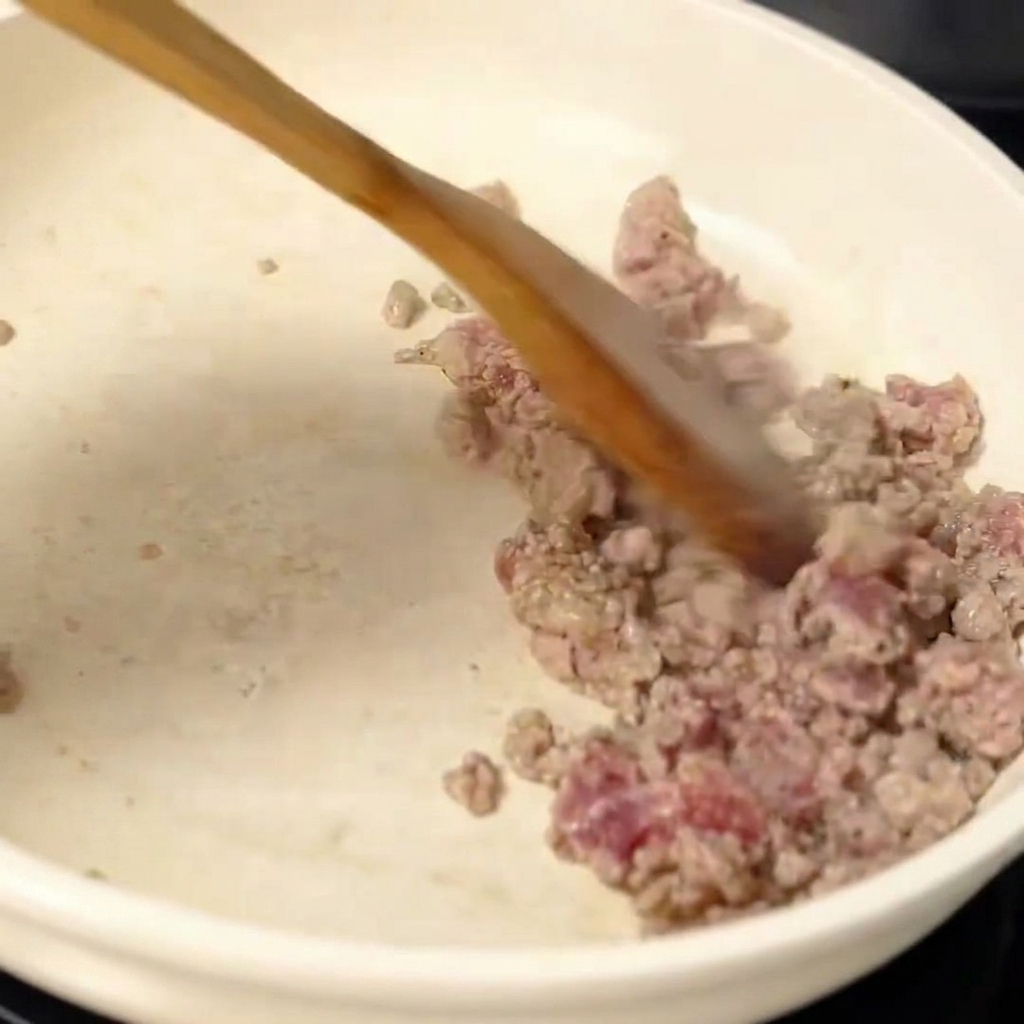 Angebratenes Hackfleisch wird in der Pfanne gewürzt.
