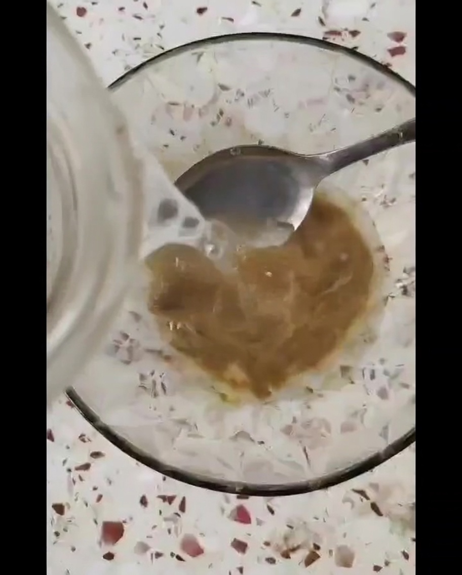 Eine kleine Glasschüssel mit einer dicken braunen Sauce, die mit einem Metalllöffel umgerührt wird.