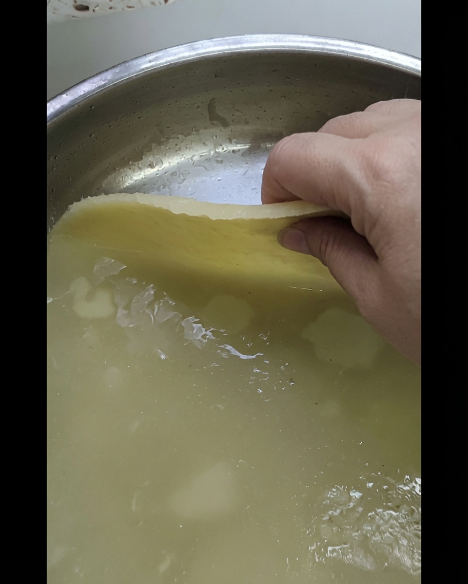 Eine Hand platziert eine ausgerollte Teigplatte auf einem glänzenden Metallblech.