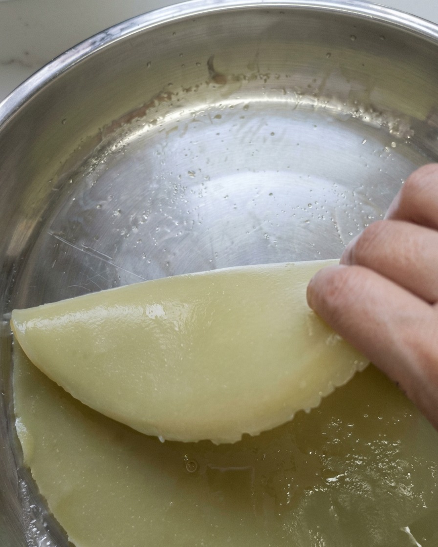 Ein Stück gedämpfter Teig wird auf einem Brett in lange, gleichmäßige Streifen geschnitten.