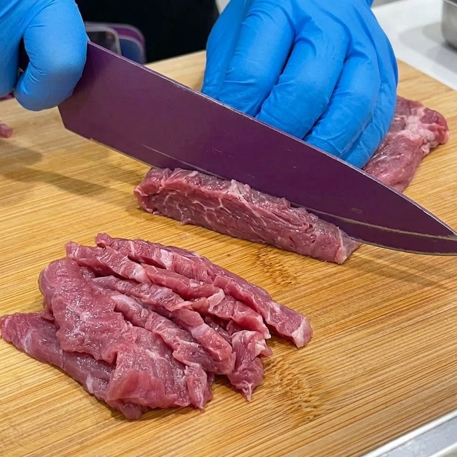 Nahaufnahme von Rindfleisch, das auf einem Holzbrett in dünne Scheiben geschnitten wird.