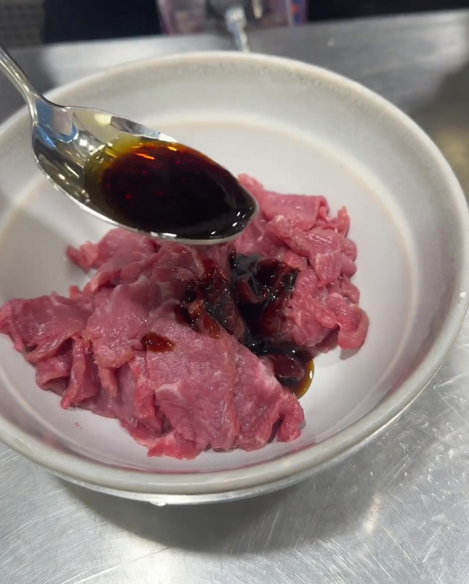 Geschnittenes rohes Rindfleisch in einer Schüssel wird mit Sojasauce, Salz, Pfeffer und Speisestärke gewürzt.
