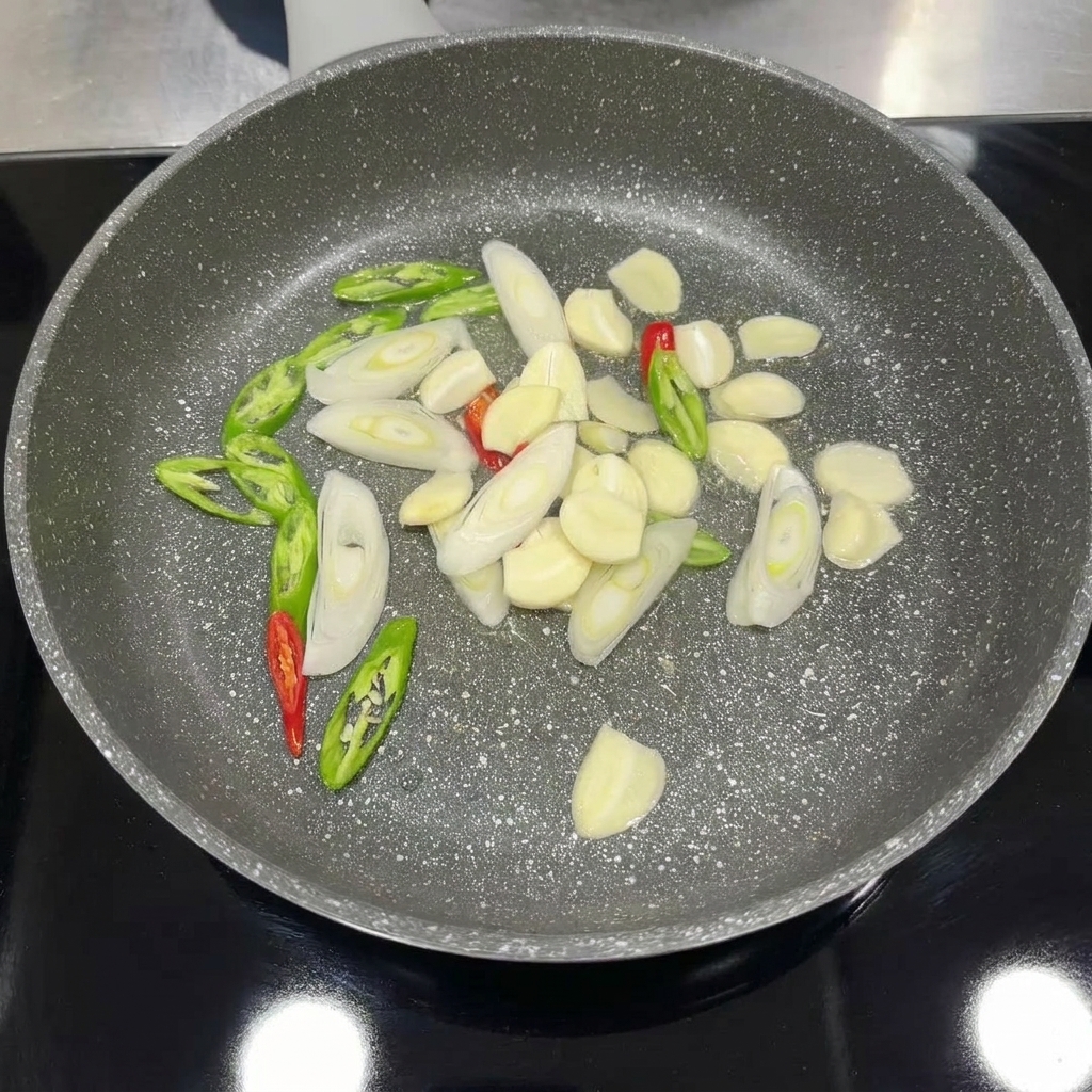 Gehackter Knoblauch, Chili und Frühlingszwiebeln werden in einer Pfanne angebraten, bis sie duften.