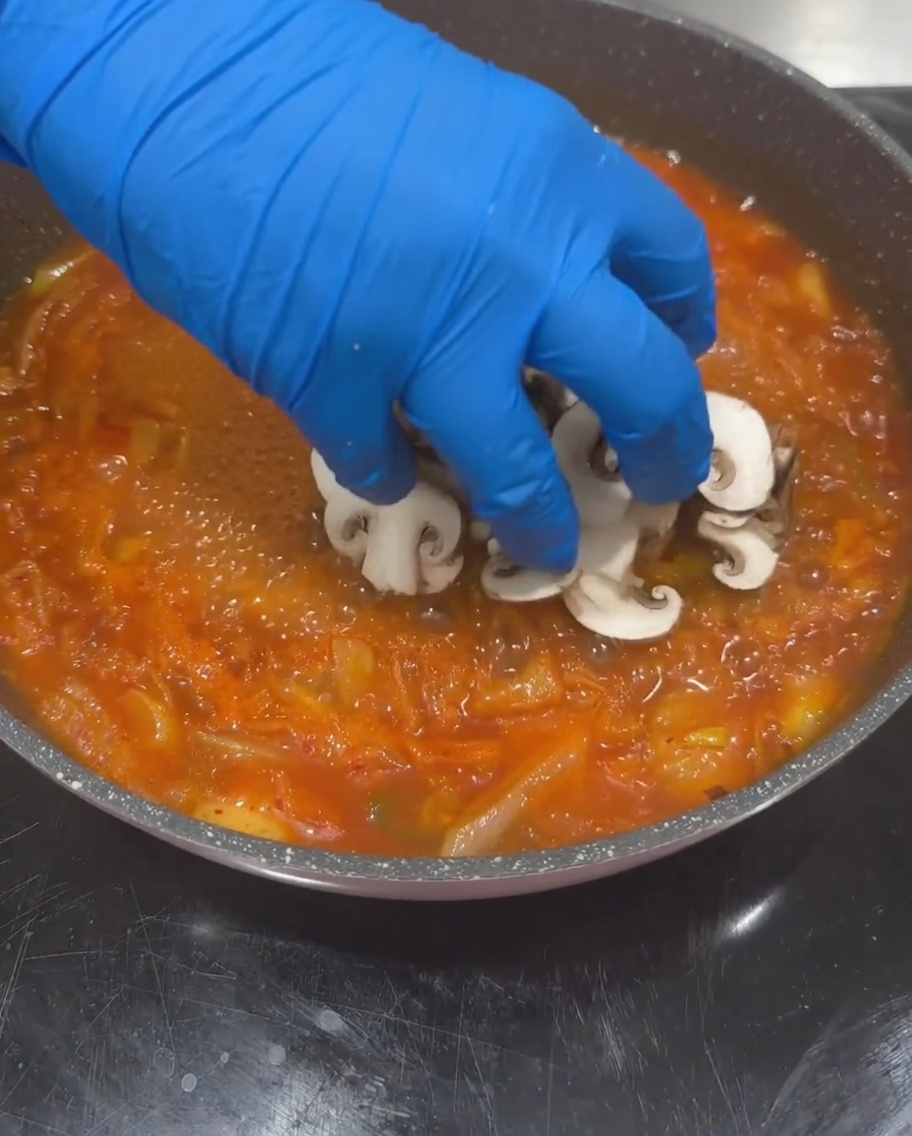 In Scheiben geschnittene Shiitake-Pilze, Zucchini und Tofuwürfel werden in die kochende Suppenbasis gegeben.