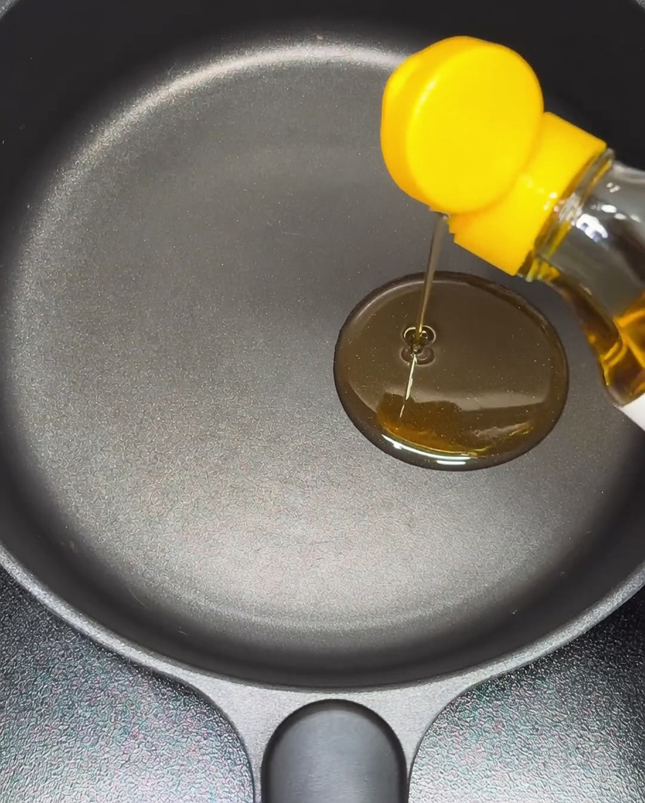 Sesamöl wird in eine beschichtete Pfanne gegossen.