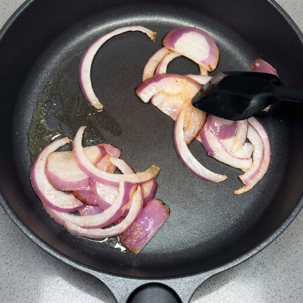 Zwiebelscheiben werden in einer Pfanne mit einem Pfannenwender geschwenkt.