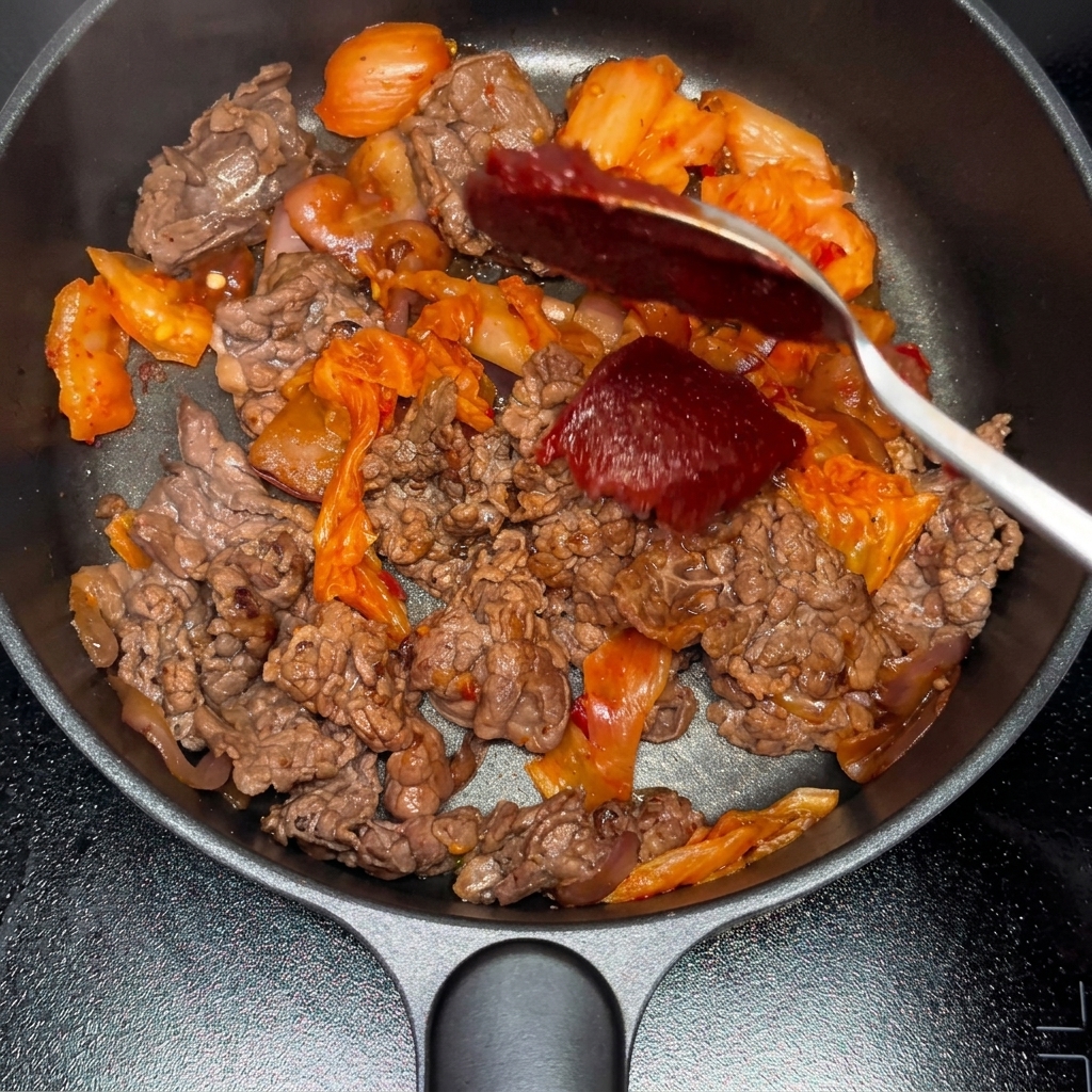 Koreanische Chilipaste und Chilipulver werden zum Rindfleisch-Kimchi-Mix gegeben.
