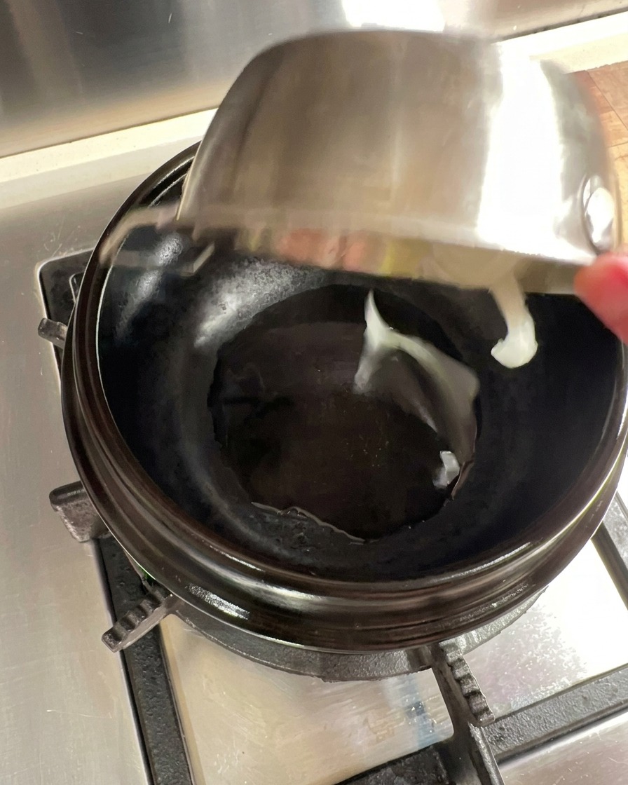 Zwiebelscheiben, die in einem vorgeheizten Steintopf mit Öl angebraten werden.