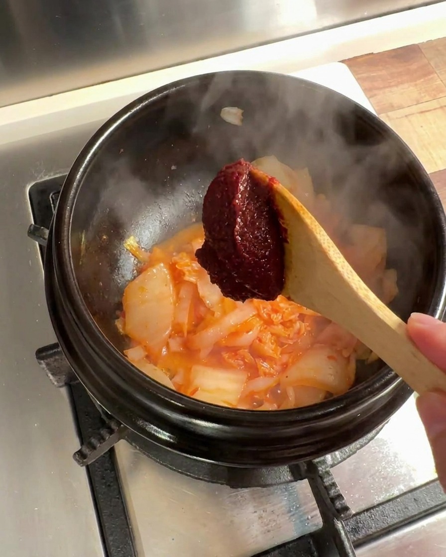 Ein Löffel koreanische Chilipaste wird zur Kimchi-Zwiebel-Mischung im Steintopf gegeben.