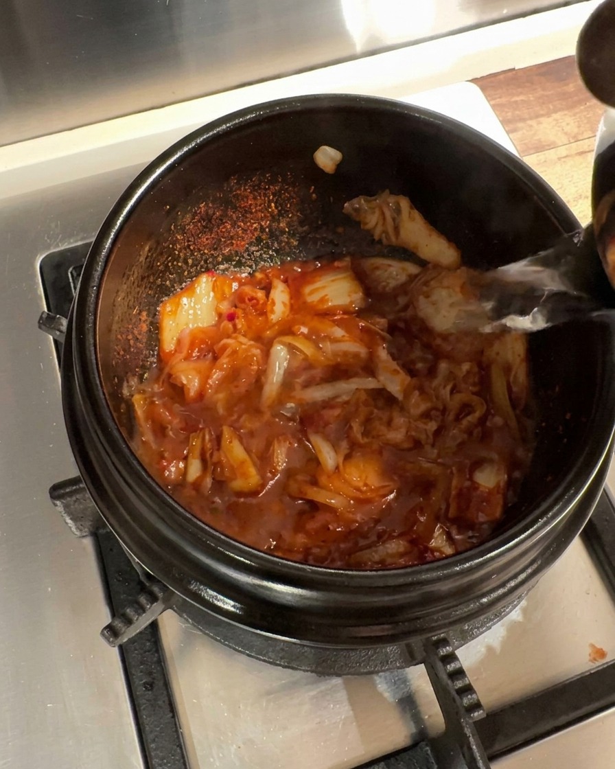 Heißes Wasser wird in den Steintopf mit der gewürzten Kimchi-Zwiebel-Mischung gegossen.