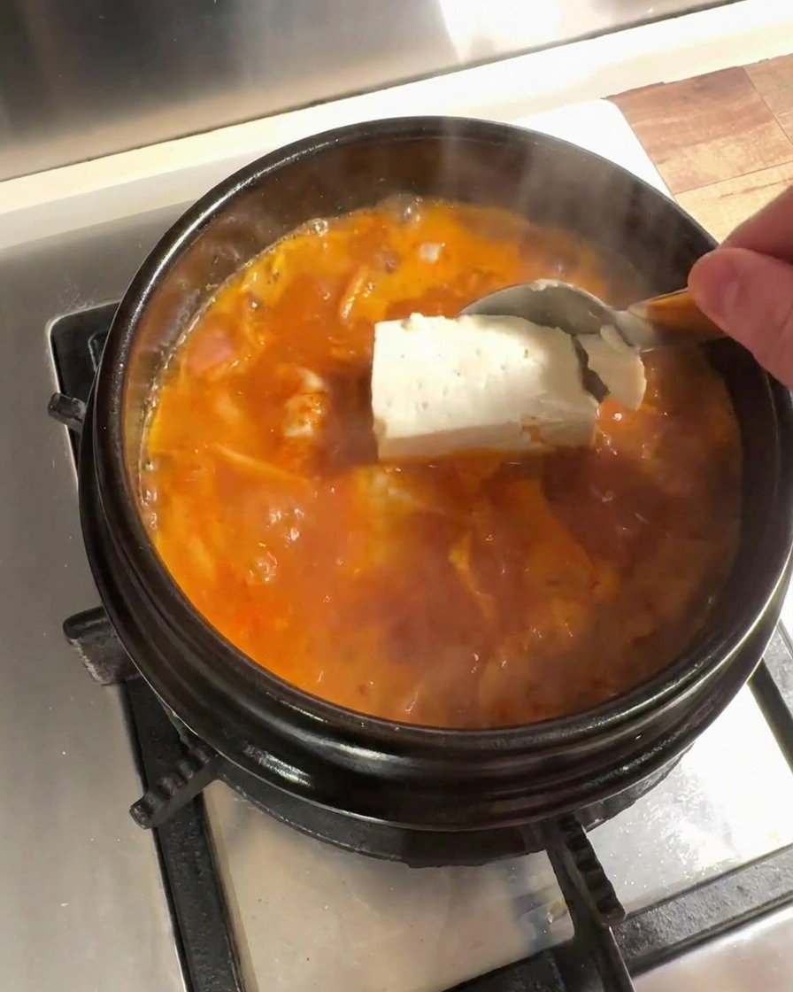 Große Stücke von frischem Tofu werden in die köchelnde Kimchi-Brühe gegeben.