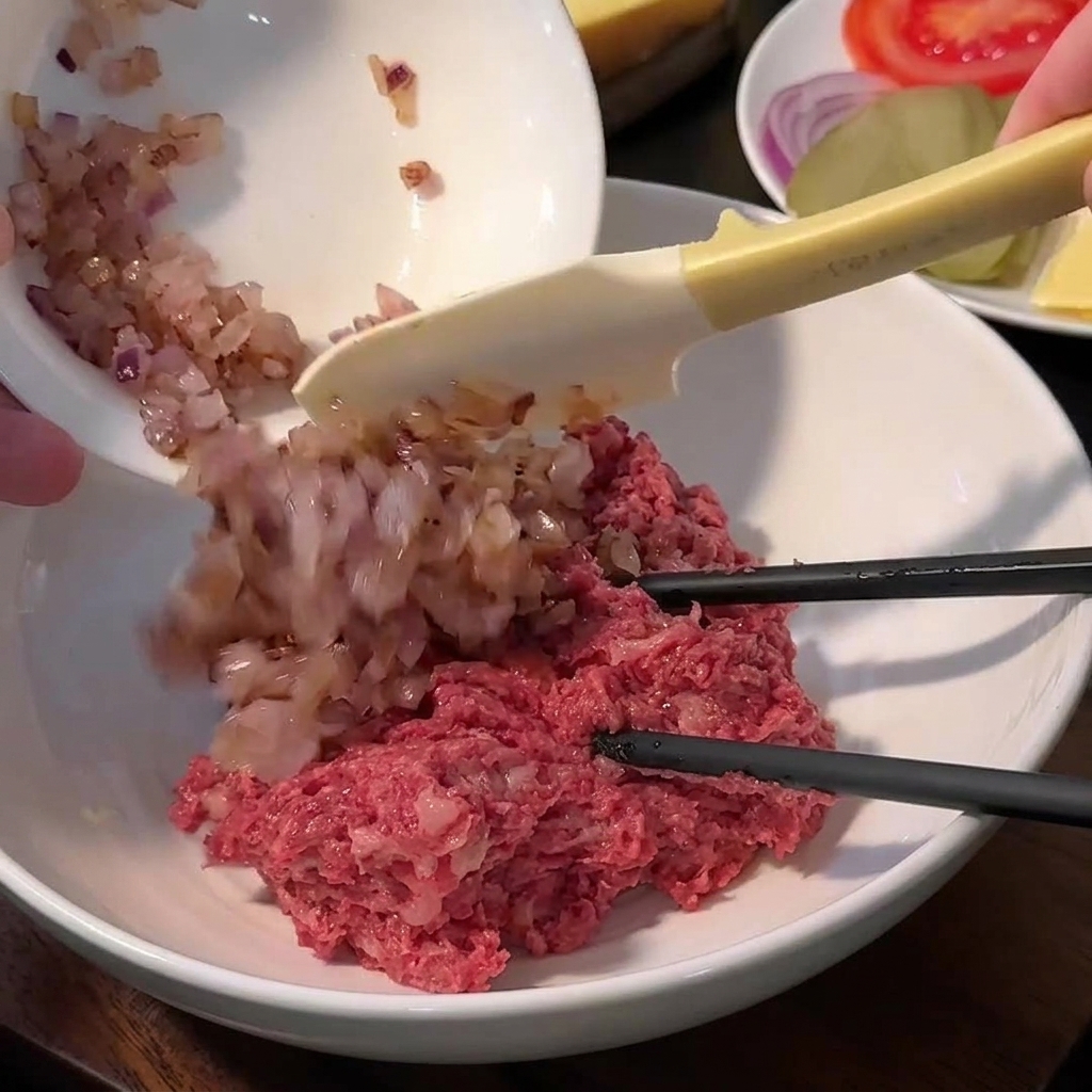 Eine Schüssel mit Hackfleisch, Semmelbröseln, Gewürzen und gedünsteten Zwiebeln vor dem Vermischen.
