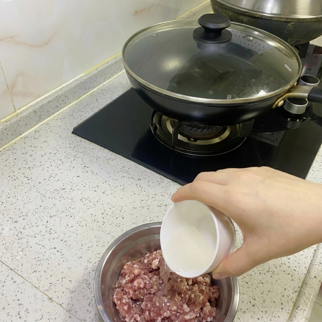 Klares Zwiebel- und Ingwerwasser wird in eine Schüssel mit rohem Schweinehackfleisch gegossen.
