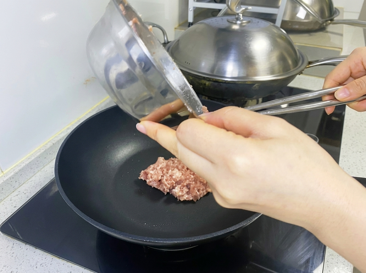 Die gewürzte, rohe Fleischmischung wird in einer schwarzen Pfanne zu einem Patty geformt.
