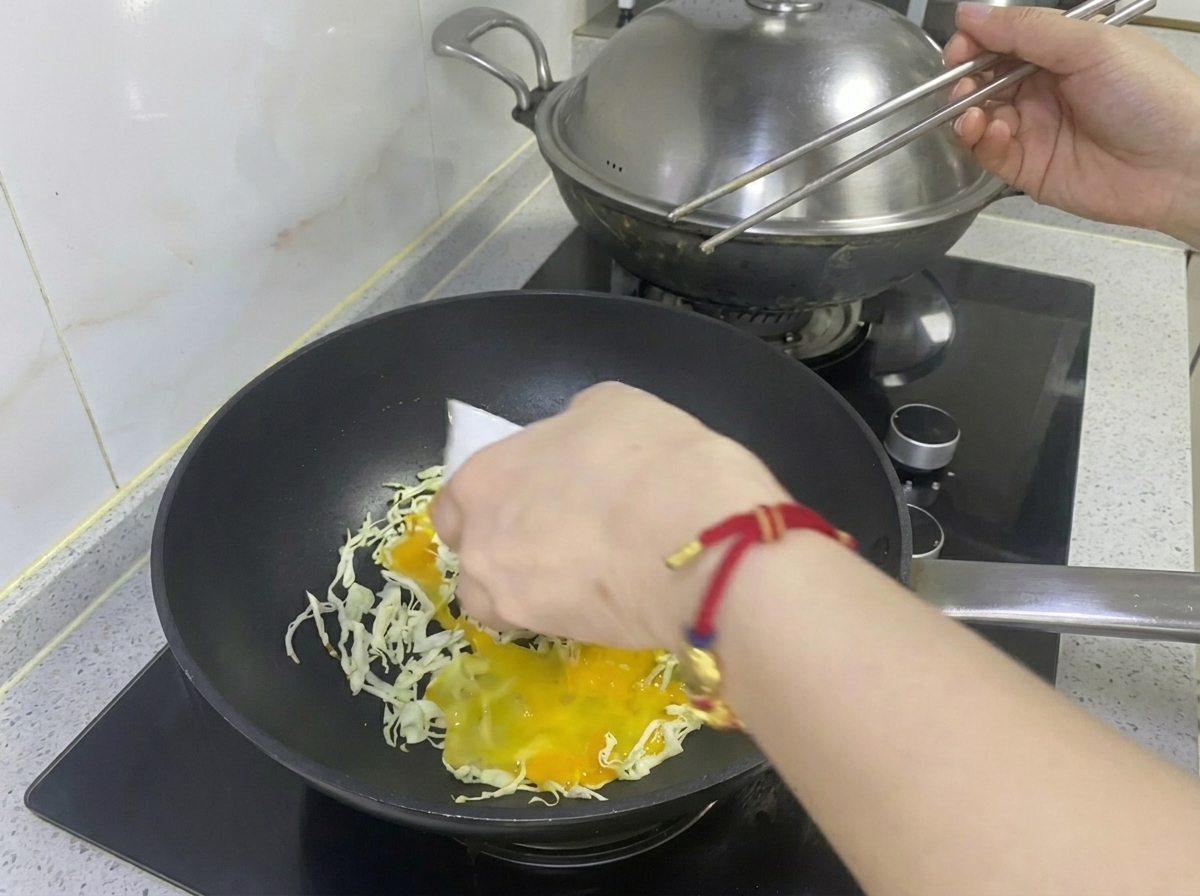 Verquirltes Ei wird über den gehobelten Kohl in der Bratpfanne gegossen.