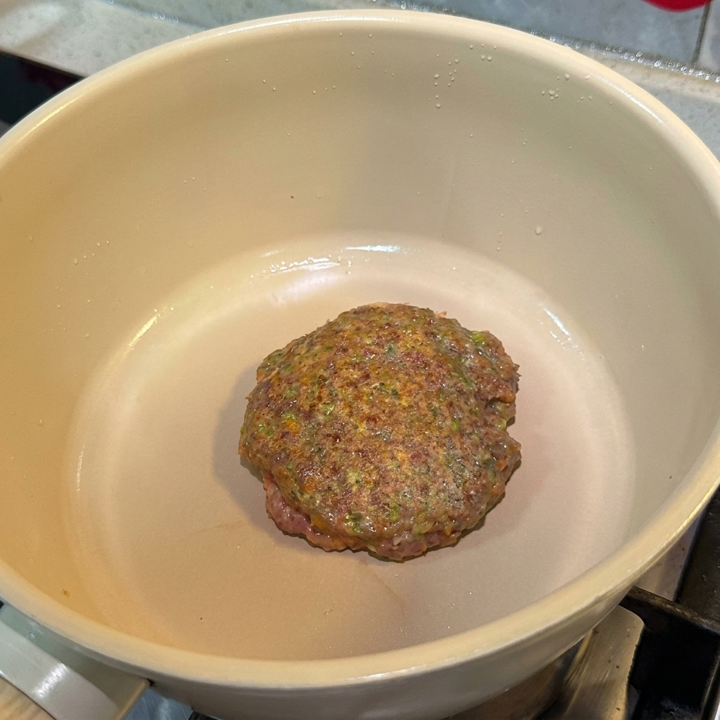 Ein gewürztes Rinder-Patty brät in der Pfanne und zeigt eine braune Oberfläche.