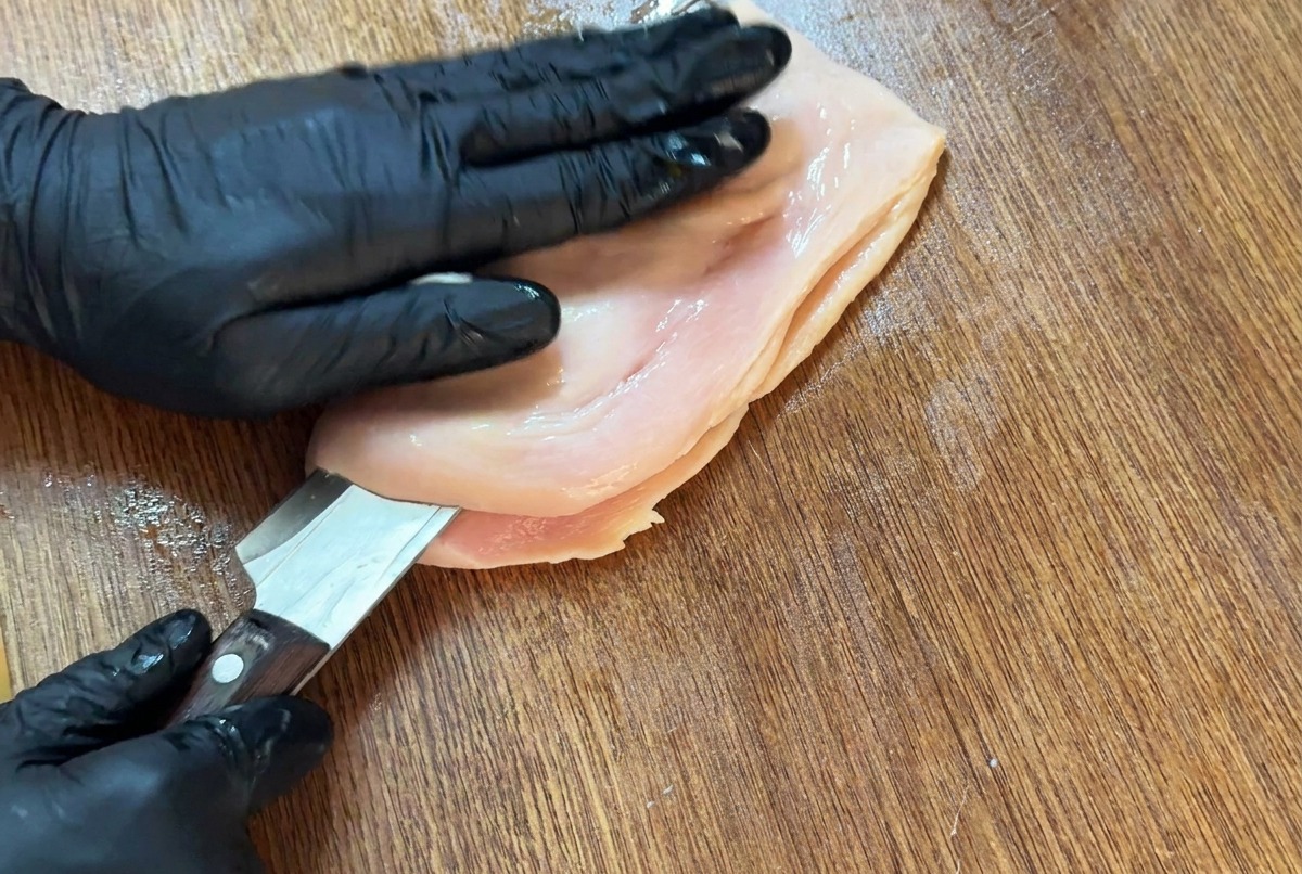 Ein scharfes Messer schneidet horizontal in die Hähnchenbrust, um sie zu schmettern.