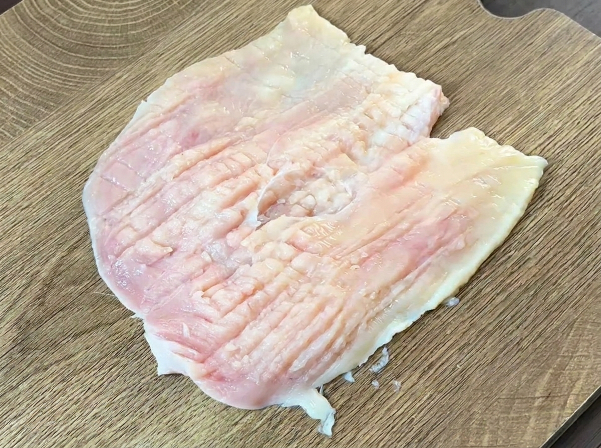 Der Rücken eines schweren Messers wird genutzt, um die Hähnchenbrust flach zu klopfen.