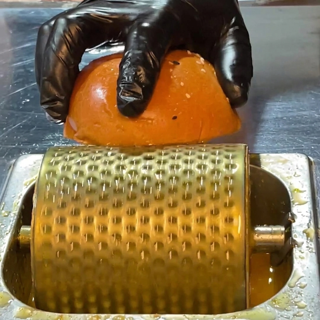 Eine behandschuhte Hand drückt eine Brötchenhälfte auf eine mit Butter bestrichene Fläche.