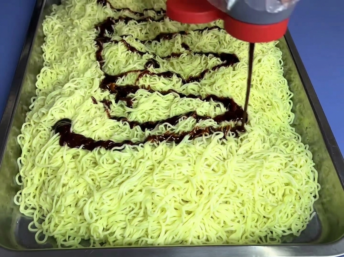 Milde Feuernudelsoße, die aus einer Flasche auf ein Nudelbett geträufelt wird.
