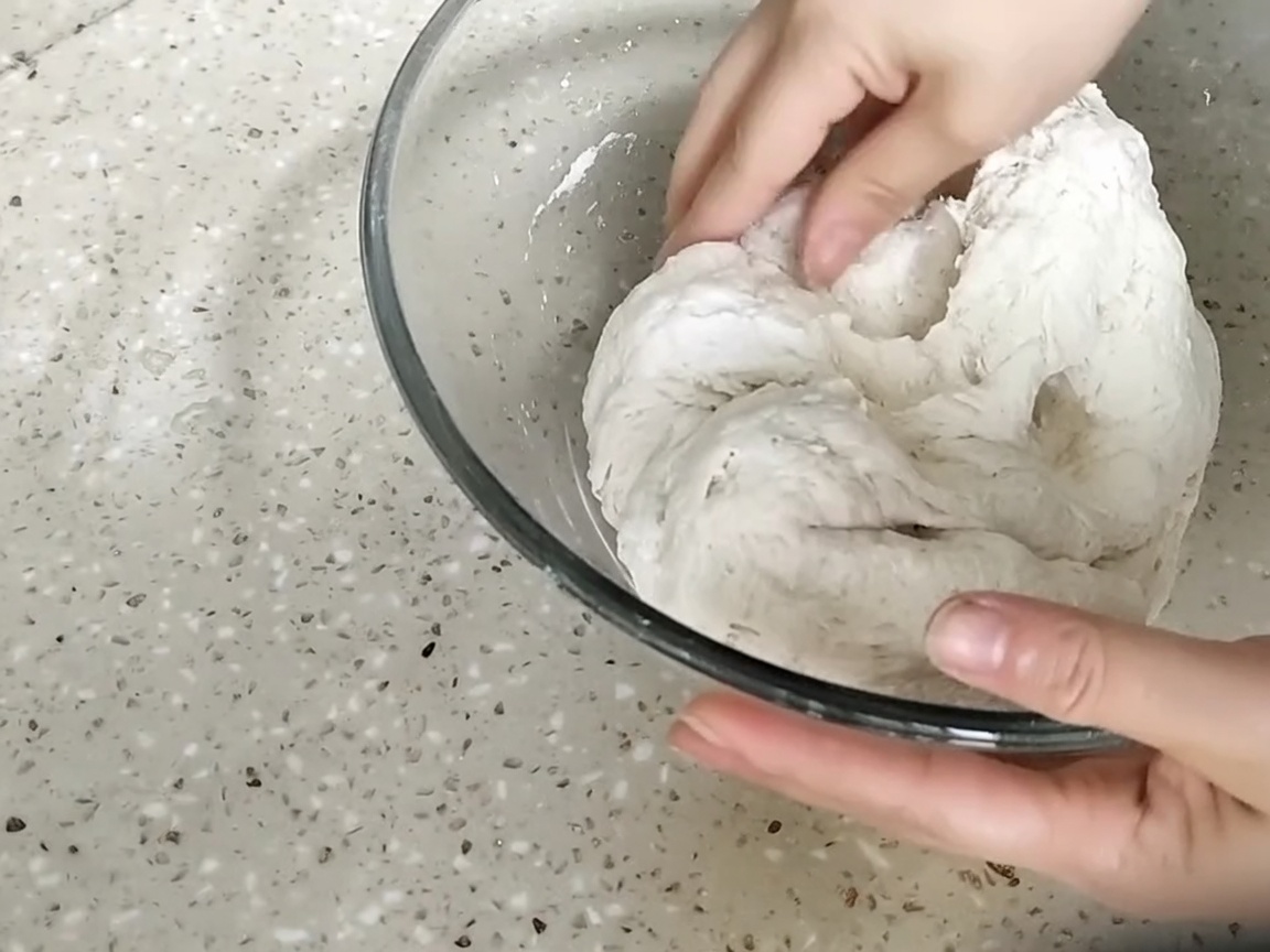 Hände kneten einen groben, zottigen Teigballen in einer Glasschüssel.