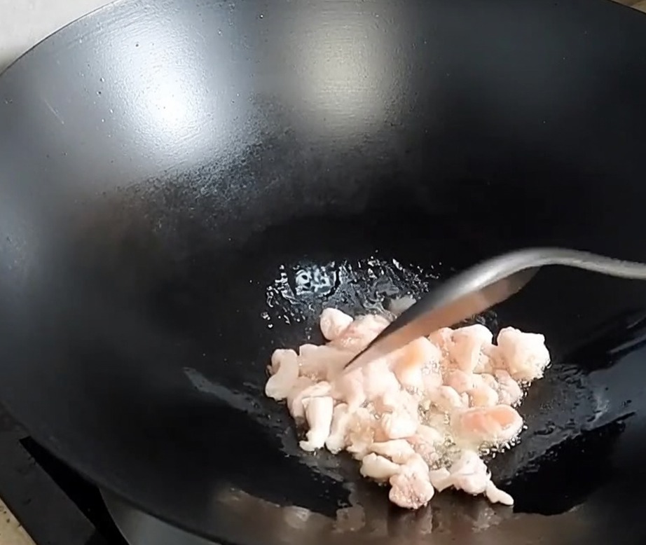Gewürfelter Schweinebauch bräunt und setzt Fett in einem heißen Wok frei.