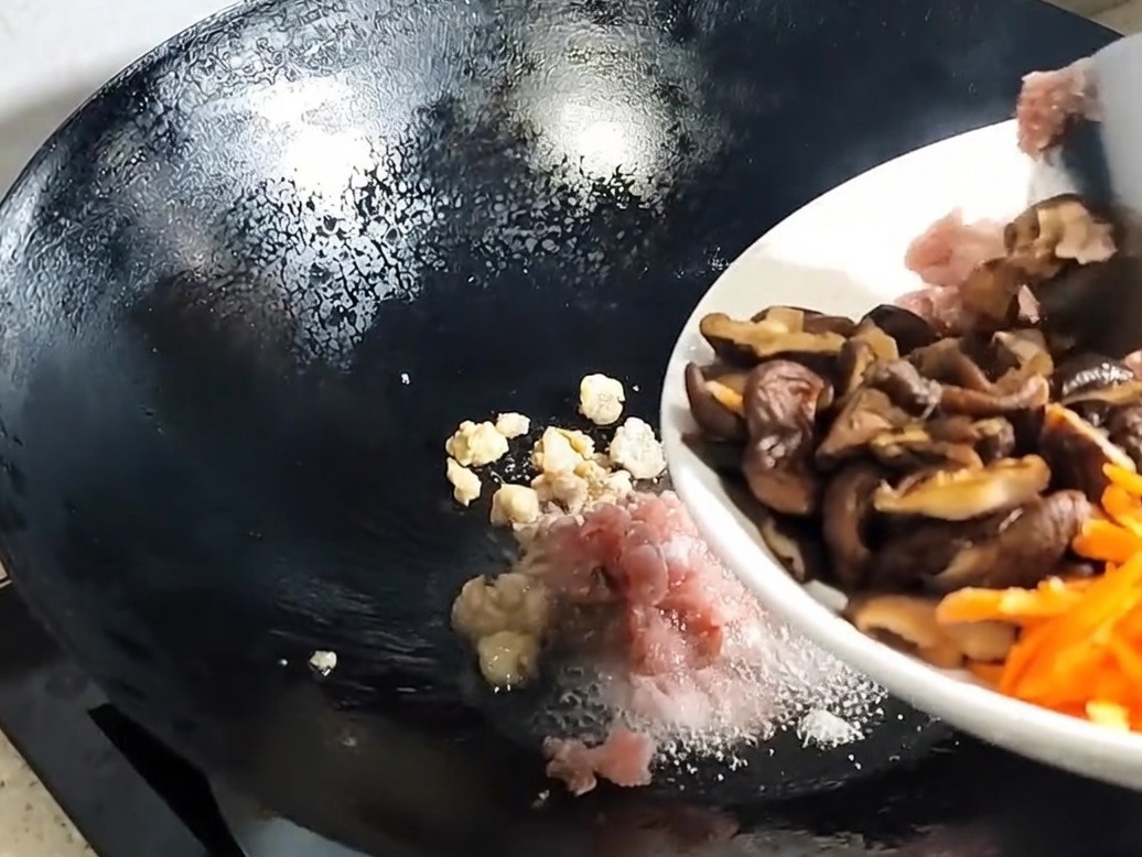 Geschnittene Shiitake-Pilze und Aromaten werden zum ausgelassenen Schweinefleisch in den Wok gegeben.