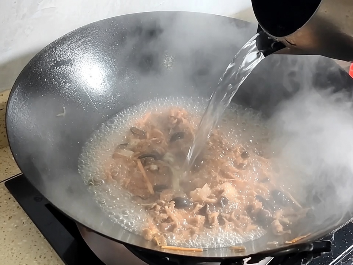 Wasser wird in den Wok mit angebratenem Schweinefleisch und Pilzen gegossen, um die Brühe zu bilden.