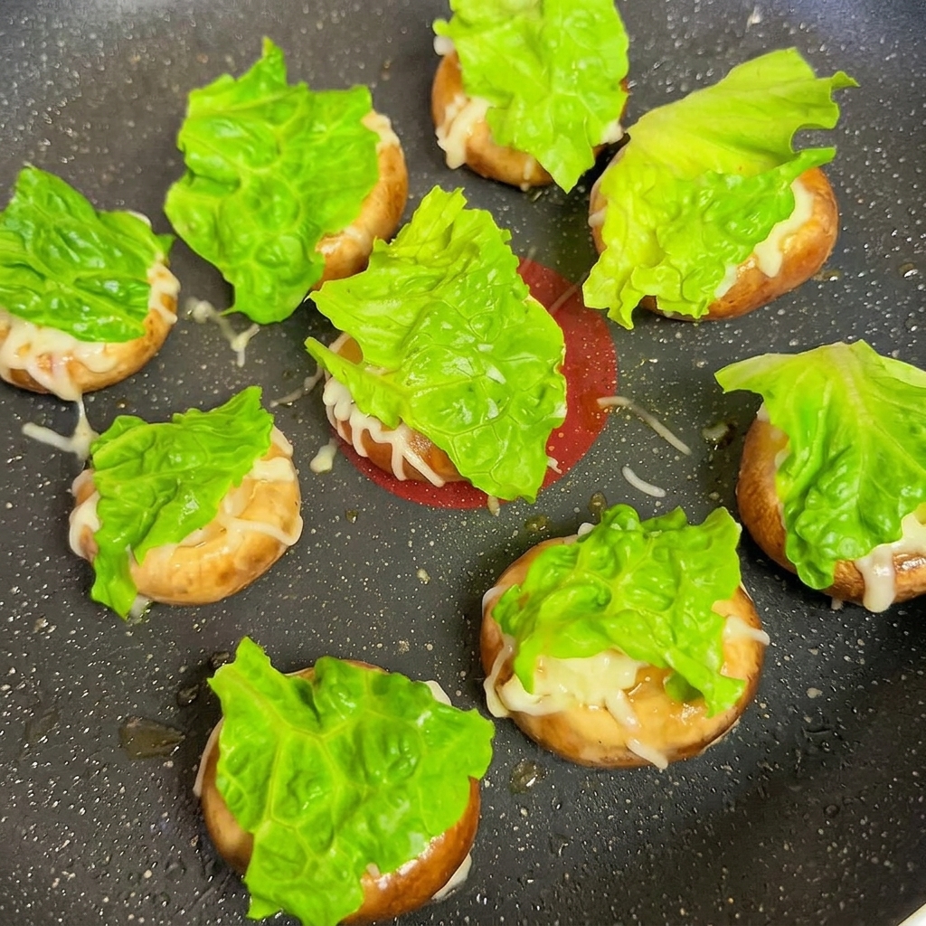 Champignonköpfe belegt mit Salat und Käsescheiben in der Pfanne.