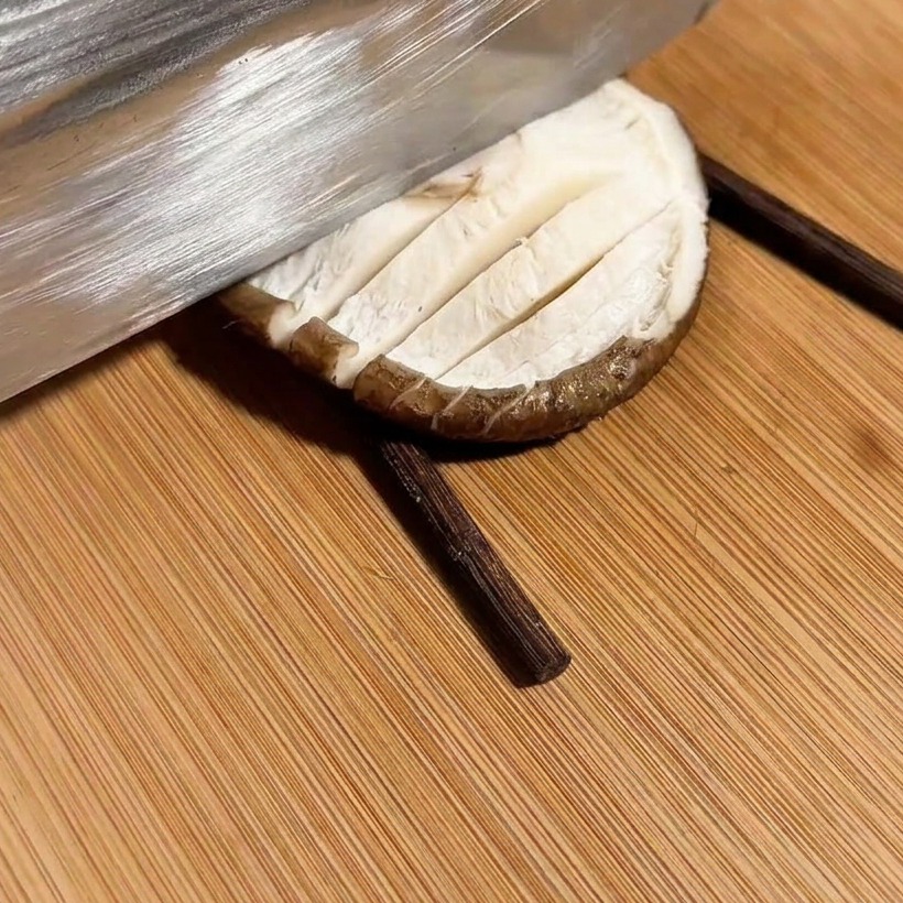 Ein Messer schneidet ein Kreuzmuster in einen Pilz, der zwischen zwei Stäbchen liegt.