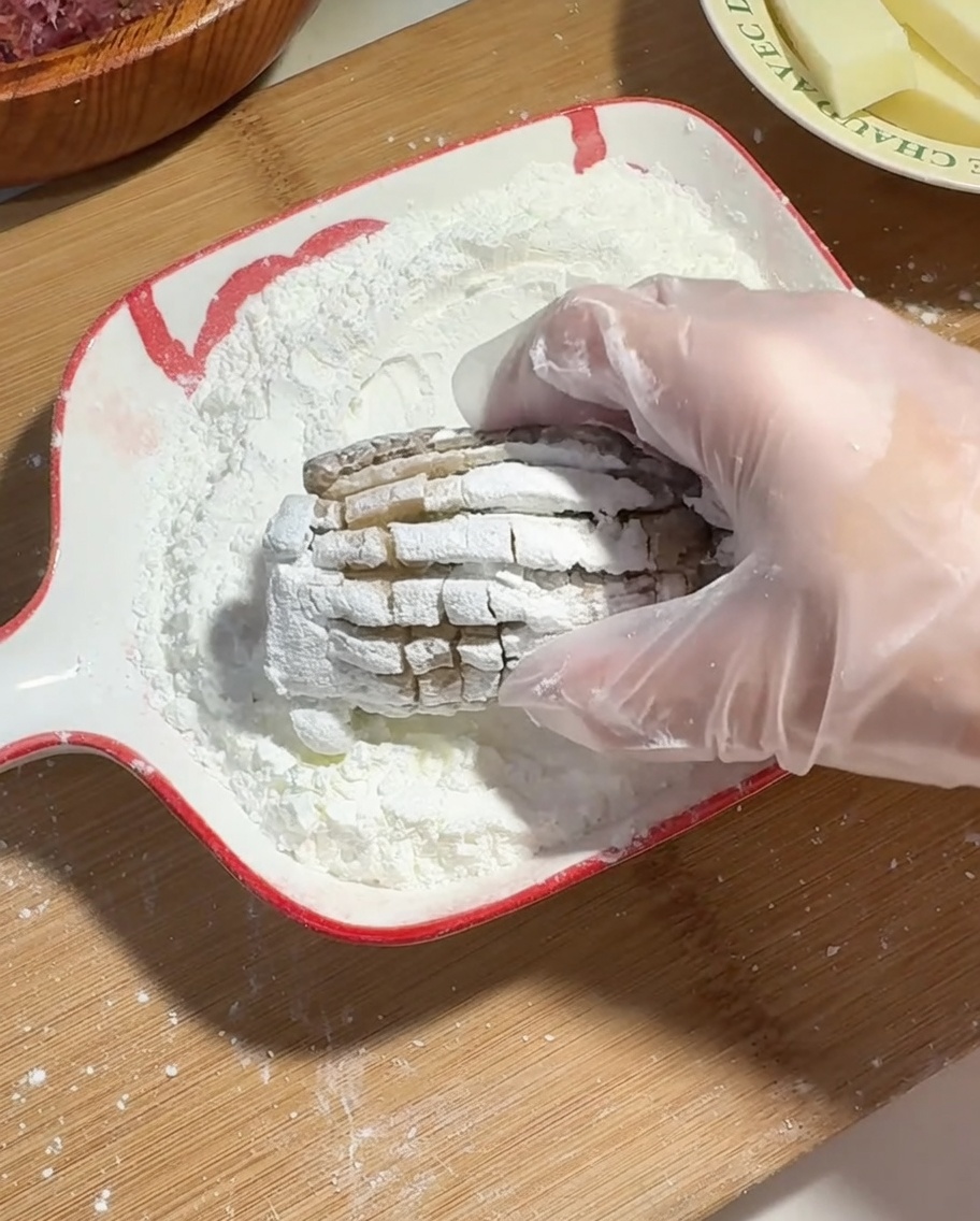 Eine Hand mit Plastikhandschuh wälzt den gefüllten Pilz in Maisstärke.