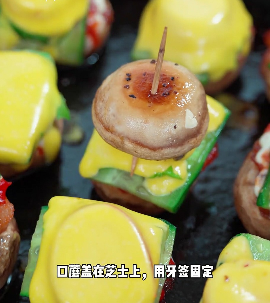Ein fertiger Mini-Pilzburger, gesichert mit einem Zahnstocher, mit den geschichteten Lagen aus Pilz, Gurke, Salat, Tomate, Käse und einem zweiten Pilzkopf.