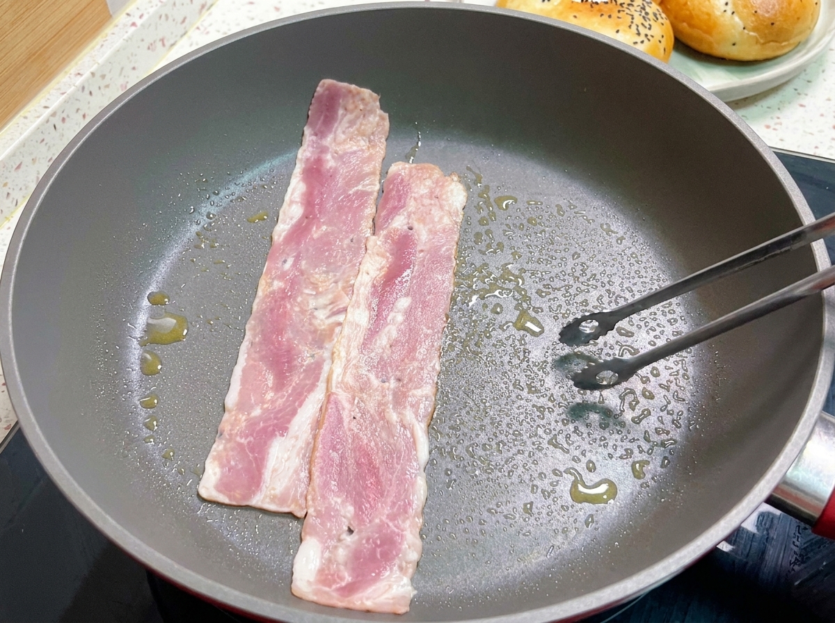 Speckstreifen braten in einer heißen Pfanne, wobei eine Scheibe mit einer Zange gewendet wird.