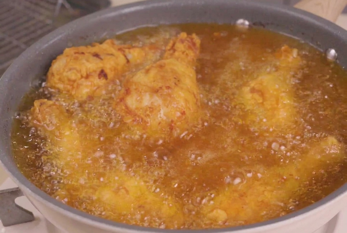 Frittierte Hähnchenteile werden für den letzten Frittiergang in eine Pfanne mit heißem, sprudelndem Öl getaucht.