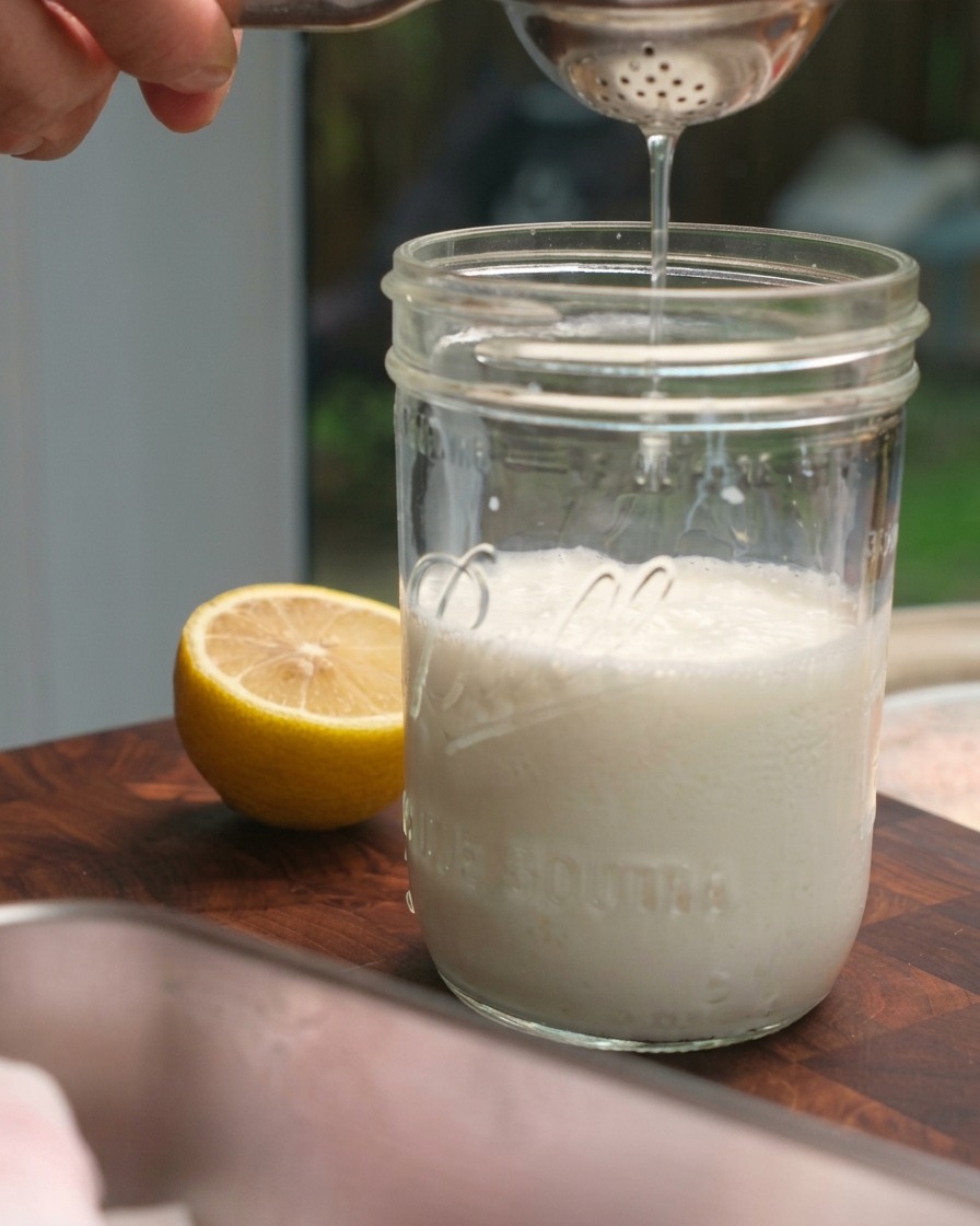 Frischer Zitronensaft wird mit einer Presse in ein Glas Milch geträufelt.