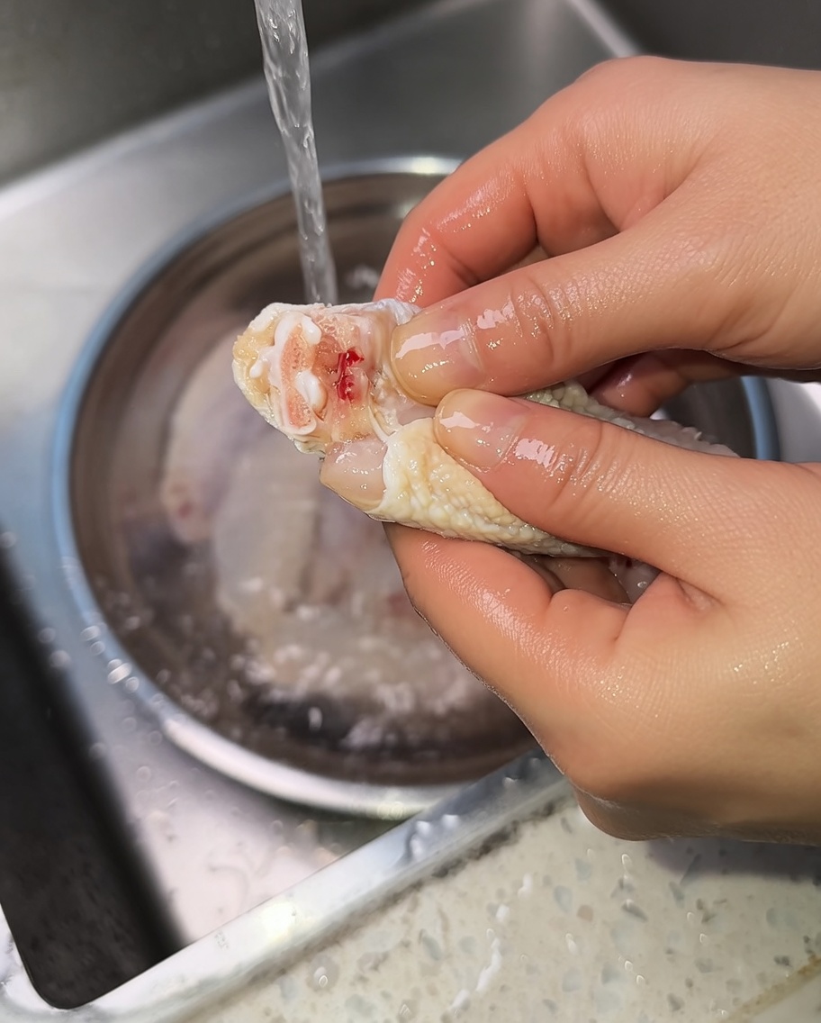 Nahaufnahme von Händen, die einen rohen Hähnchenflügel ausdrücken, um Blut aus dem Gelenk zu entfernen.