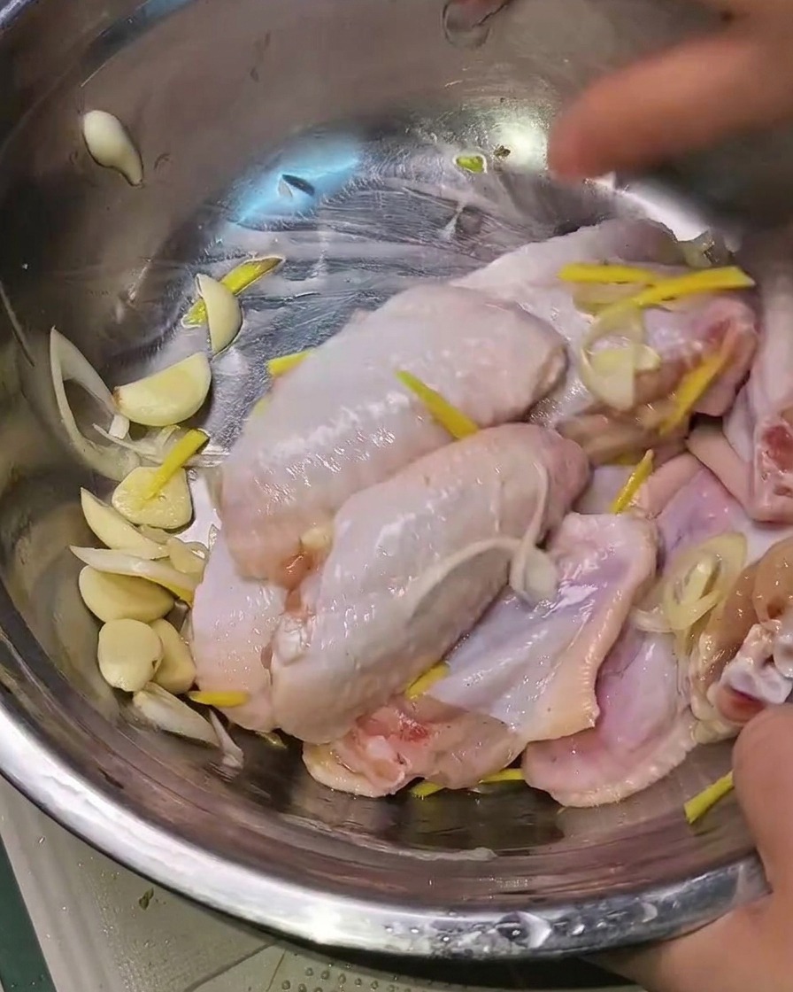 Hände beim Vermischen der marinierten Hähnchenflügel mit den Aromaten.
