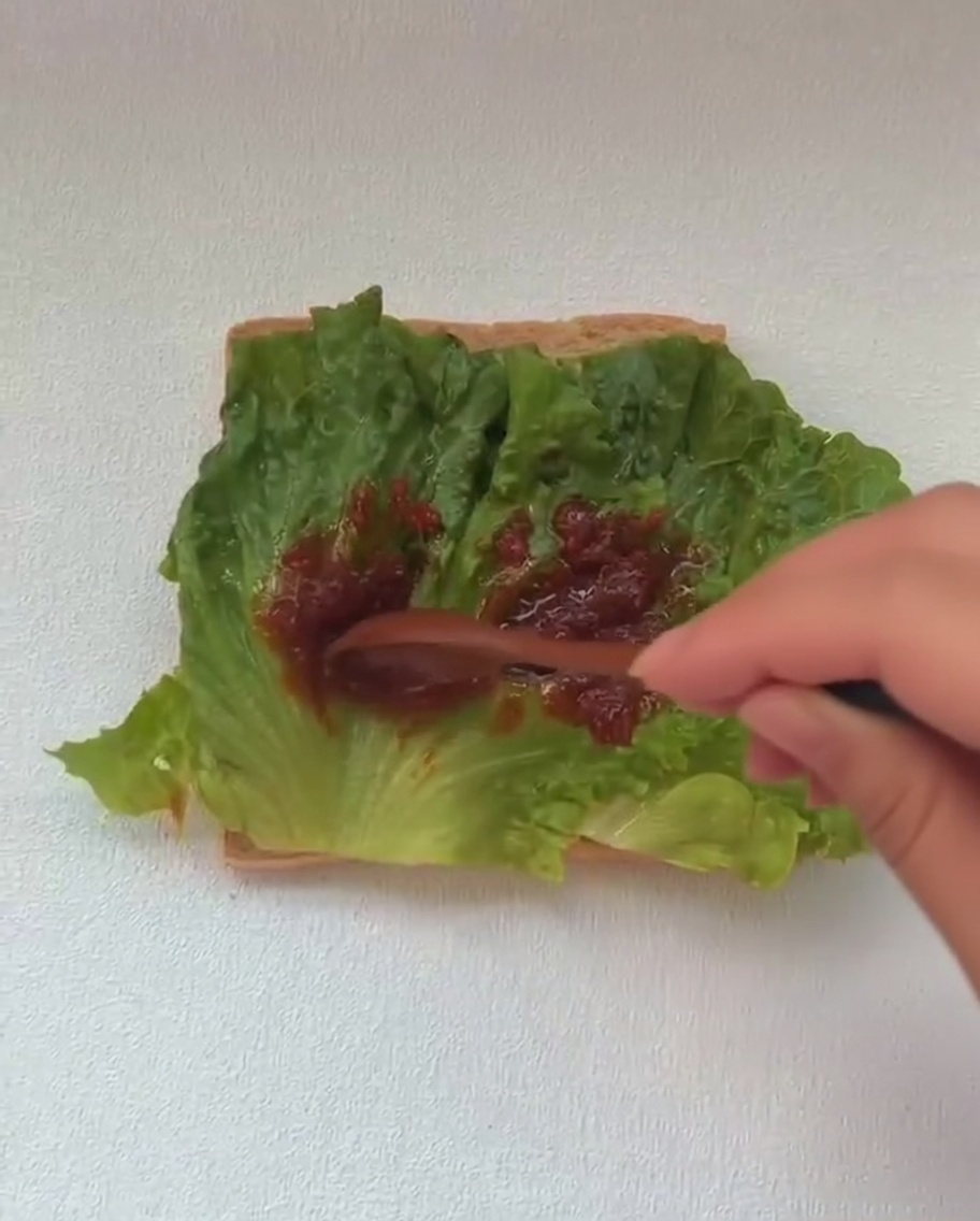Ein frisch gebratenes Spiegelei wird auf das Sandwich geschichtet und liegt auf dem grünen Salat.