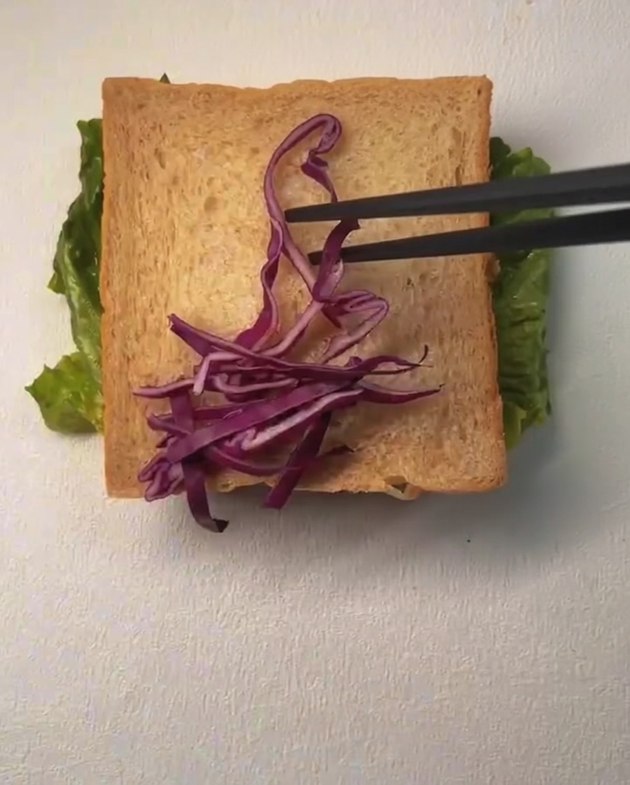 Eine Toastscheibe wird mit geraspeltem Rotkohl und Maiskörnern belegt, darüber wird Mayonnaise geträufelt.