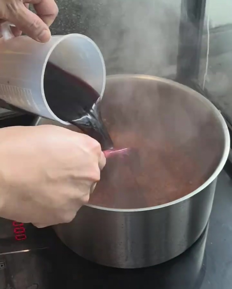 Rotwein wird aus einem Messbecher in den Topf gegossen.