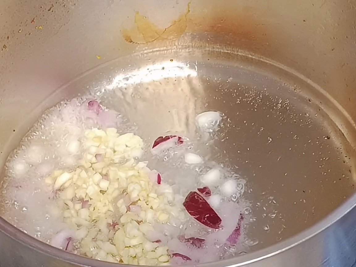 Gehackte rote Zwiebeln und Knoblauch brutzeln in heißem Öl in einem Metalltopf.