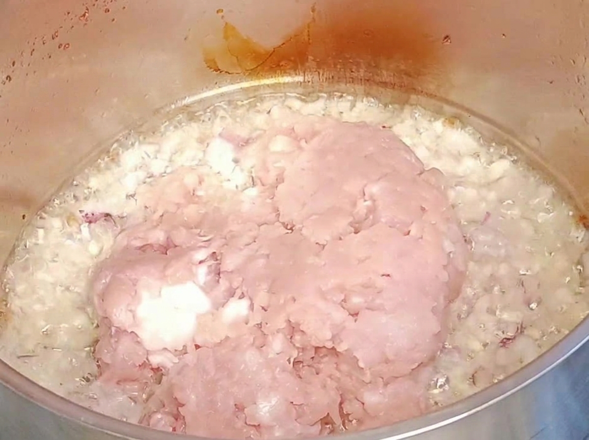Rohes Hackfleisch wird über die angebratenen Zwiebeln und den Knoblauch in einen Metalltopf gegeben.