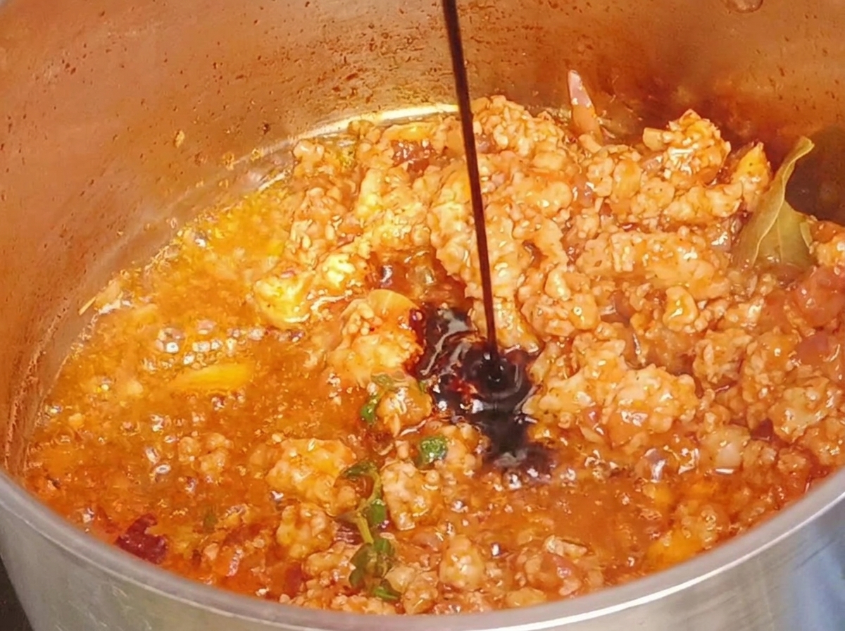 Dunkle Sojasoße wird in einen Topf mit gekochtem, rötlichem Hackfleisch gegossen.