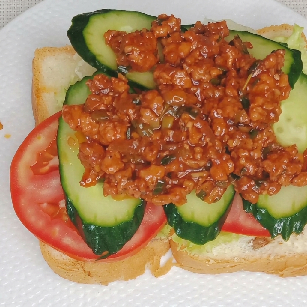 Nahaufnahme von cremiger Eigelbsoße, die über die Fleischsoßenschicht auf einem Sandwich geträufelt wird.