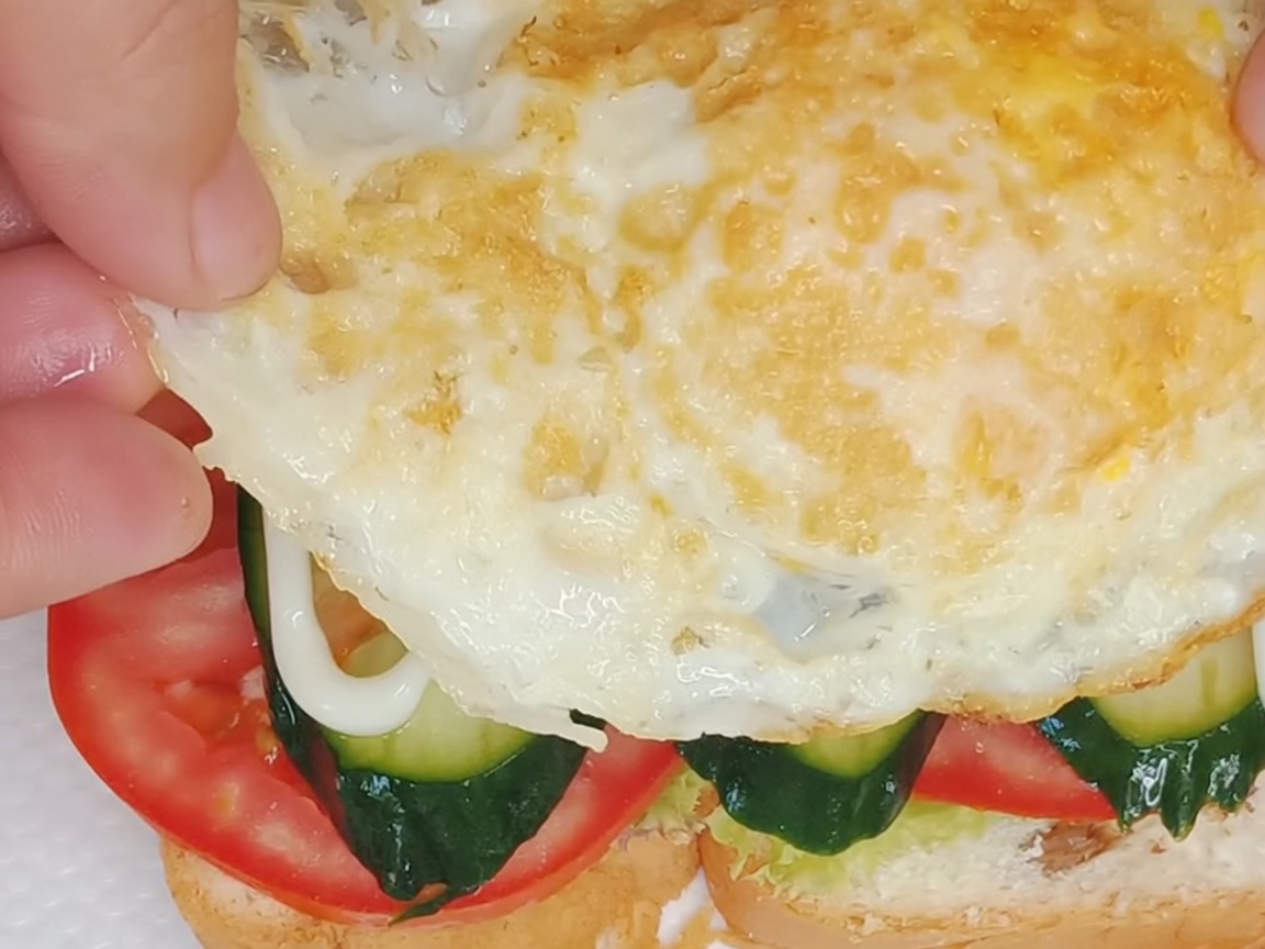 Ein perfekt gebratenes Spiegelei wird vorsichtig auf die zusammengesetzten Sandwichschichten gelegt.