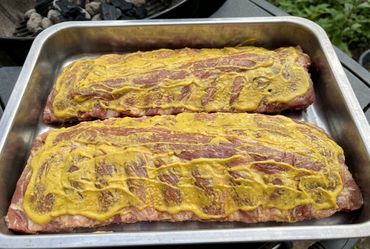 Zwei mit gelber Sauce bestrichene Rippchen liegen auf dem Grillrost und werden geräuchert.