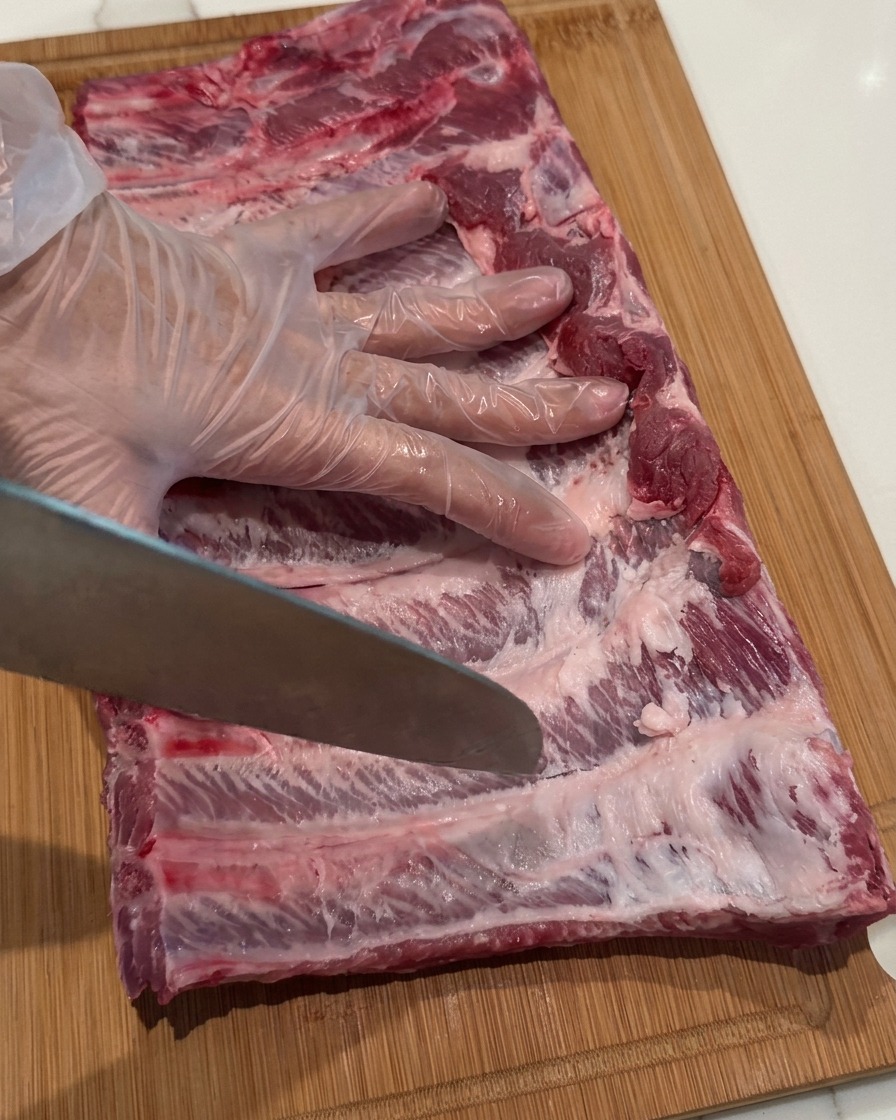 Eine Hand mit Handschuh sticht mit einer Messerspitze kleine Löcher in die rohen Rippchen.
