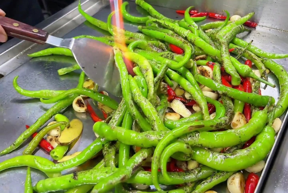 Knoblauchzehen und rote Chilis werden mit einem Flammbrenner auf einer Grillplatte angekohlt.