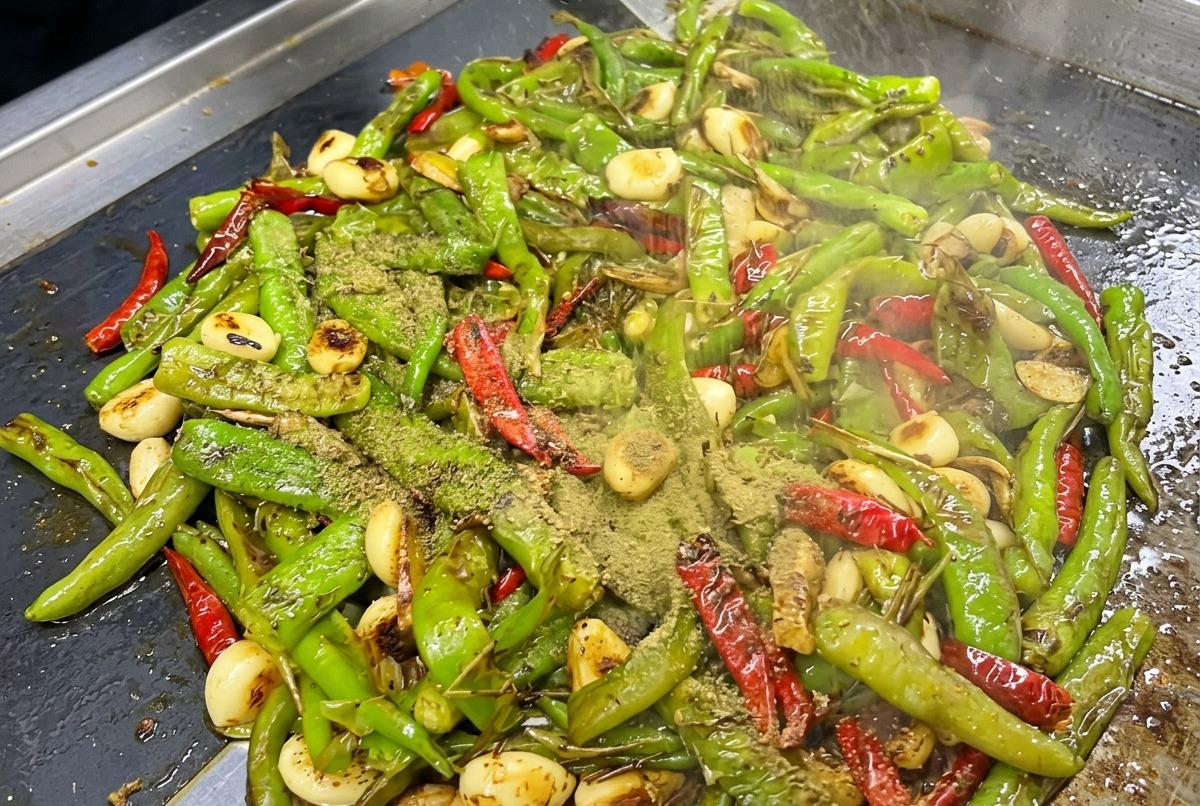 Gewürze und Soßen werden über die gerösteten Paprika auf der Grillplatte gestreut.