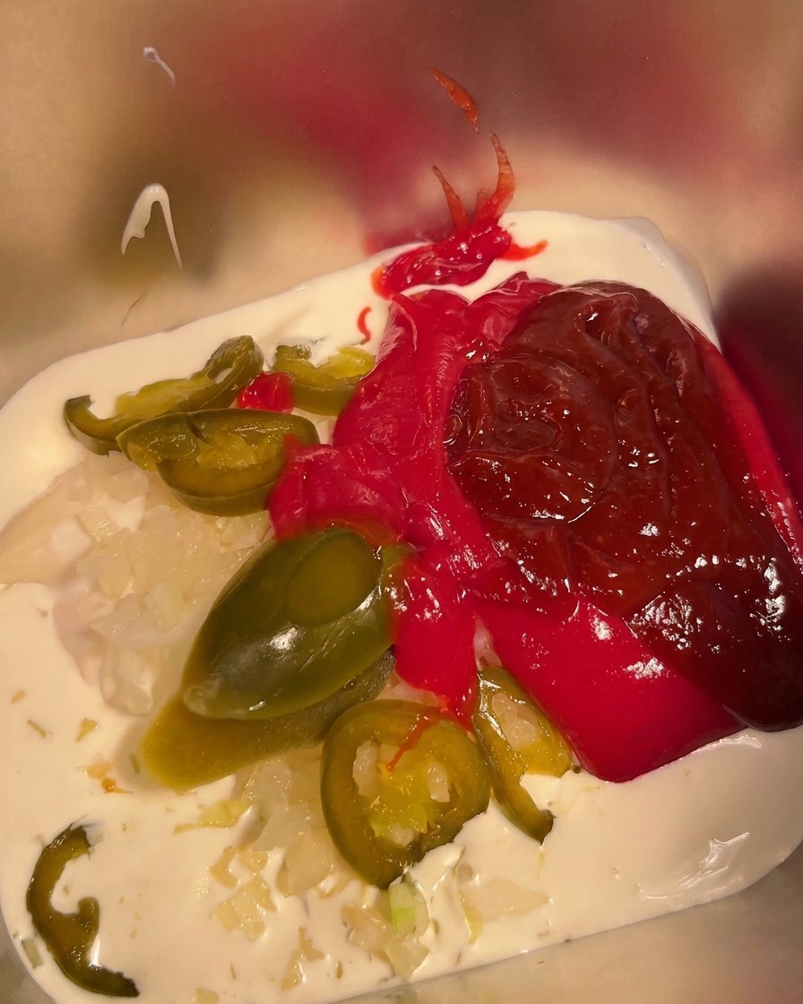 Chilipulver wird über die Mischung im Metallbehälter gestreut.